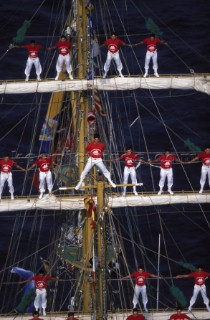 Classic ketch yacht sailing behind an outcrop of rock  Classic ketch yacht sailing behind an outcrop of rock  Sailors standing along yard arms of square rigger Gloria - Monaco Classic Week 1997