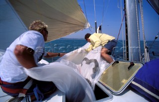 Two crew members take down a spinnaker and store it below ready for the next downwind leg of a race