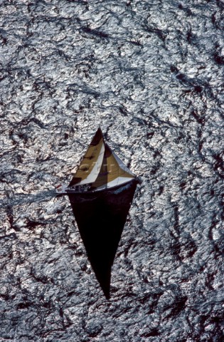 A sailing yacht casts a shadow on textured sunlit water