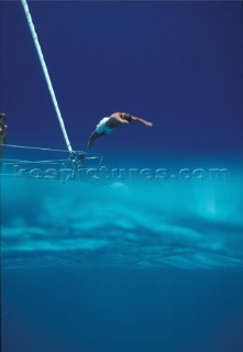 Man diving off bow of yacht into clear blue water