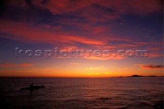 Canoeist paddling against a crimson sunrise sky, Baja, California