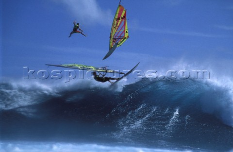 A windsurfer jumps off a wave while another falls from his rig in mid air