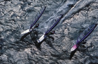 Three windsurfers race across the water