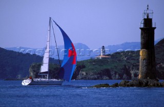 Cruising yacht sailing past a lighthouse into a sheltered bay