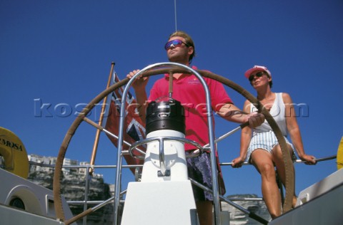 Woman sitting behind man helming cruising yacht