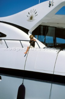 Boy sits on rail of motor yacht