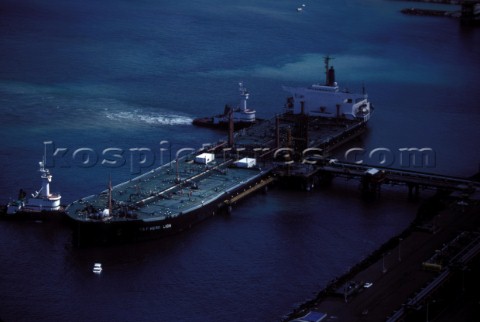 Laden oil tanker is pushed into its docking position by two tug boats