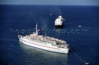 One cruise ship moored to a buoy while another makes a turn underway