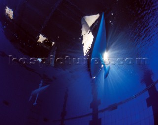 Model yachts racing in a blue swimming pool shot from underwater with lighting, showing keels and rudders