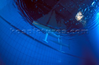 Model yachts racing in a blue swimming pool shot from underwater with lighting, showing keels and rudders