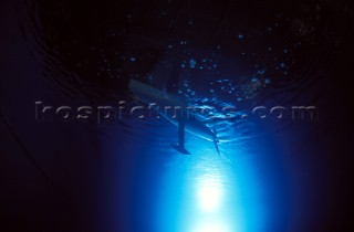 Model yachts racing in a blue swimming pool shot from underwater with lighting, showing keels and rudders