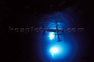 Model yachts racing in a blue swimming pool shot from underwater with lighting, showing keels and rudders