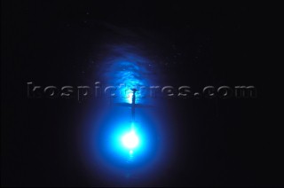 Model yachts racing in a blue swimming pool shot from underwater with lighting, showing keels and rudders