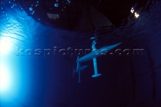 Model yachts racing in a blue swimming pool shot from underwater with lighting, showing keels and rudders