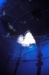 Model yachts racing in a blue swimming pool shot from underwater with lighting, showing keels and rudders