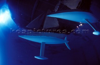 Model yachts racing in a blue swimming pool shot from underwater with lighting, showing keels and rudders