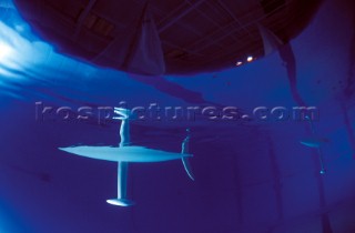 Model yachts racing in a blue swimming pool shot from underwater with lighting, showing keels and rudders