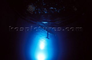 Model yachts racing in a blue swimming pool shot from underwater with lighting, showing keels and rudders