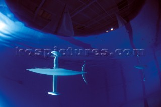 Model yachts racing in a blue swimming pool shot from underwater with lighting, showing keels and rudders