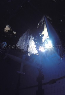 Model yachts racing in a blue swimming pool shot from underwater with lighting, showing keels and rudders