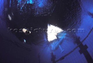 Model yachts racing in a blue swimming pool shot from underwater with lighting, showing keels and rudders