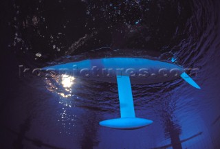 Model yachts racing in a blue swimming pool shot from underwater with lighting, showing keels and rudders