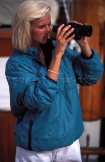Woman looking through binoculars on board classic yacht  Man on boat using hand-held GPS instrument  Woman looking through binoculars on board classic yacht