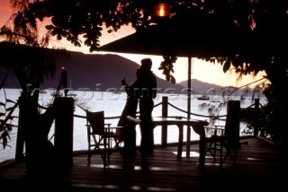 Couple standing on deck of luxury villa looking out over the bay at sunset