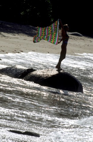 Woman standing on rock on sandy beach as tide comes in