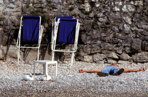 Man lying on beach next to two deckchairs