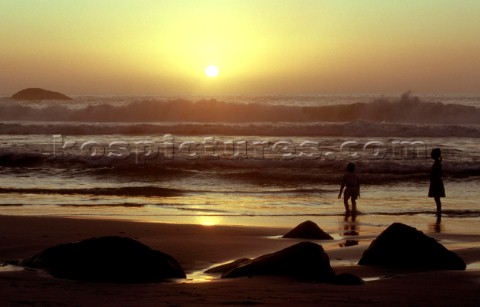 Two children standing in surf on beach at sunset