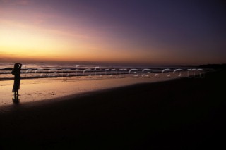 Woman on beach gazing out to sea at sunset