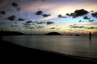 A single dinghy sailing by a deserted beach at sunset