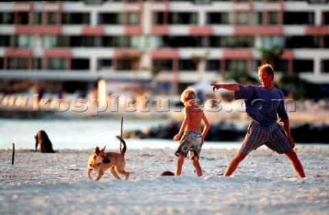 A father and son play with their dog on a sandy beach