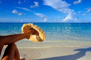 Model sits under umbrella on tropical beach.