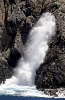 Spray from a crashing wave is forced up the gap in a cliff