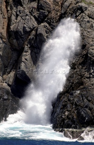 Spray from a crashing wave is forced up the gap in a cliff