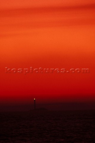 Lighthouse on rocks under red sky