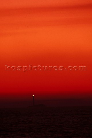 Lighthouse on rocks under red sky