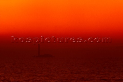 Lighthouse on rocks under red sky