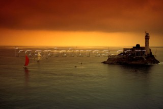 Racing yachts approach the Fastnet rock at dawn under spinnaker