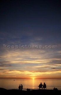 People on beach watching sunrise over calm sea.