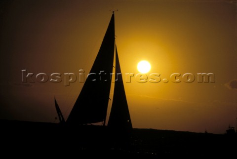 Sun behind silhouette of sails in moody sky 