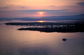 Silhouette of fishing boat heading out to sea at daybreak