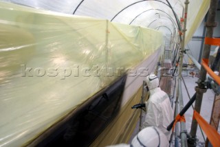 Boatyard workers painting the topsides of a superyacht with a spray gun