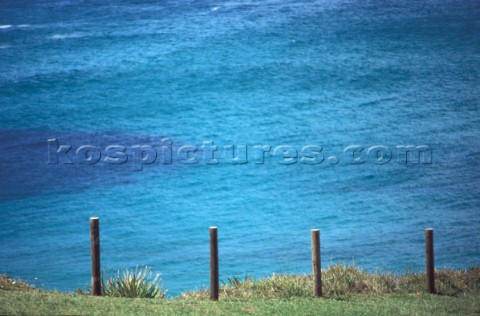 Wooden fence at edge of cliff by clear blue sea 
