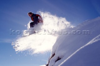 Snowboarder jumps off snowy ledge.