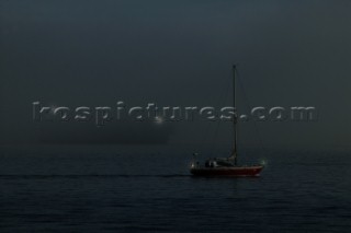 Cruising yacht motoring under power on a calm sea at night showing navigation lights on a collision course with a large commercial container ship in bad visibility and fog