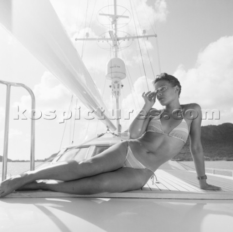 Woman on bikini sunbathing on deck of sailing superyacht