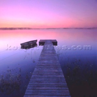 Boat moored at end of wooden jetty at sunset.